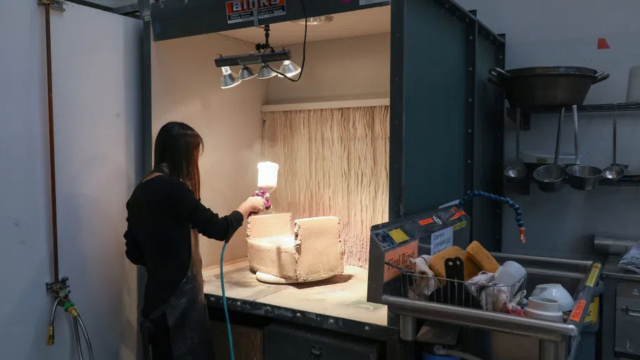 A student spraying glaze onto her Ceramics object.