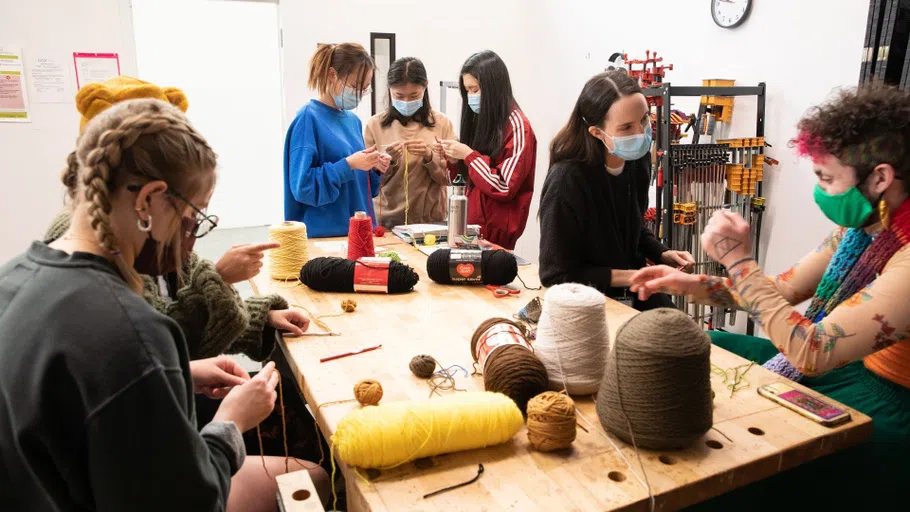 A group of students weaving colorful yarn in a classroom setting.