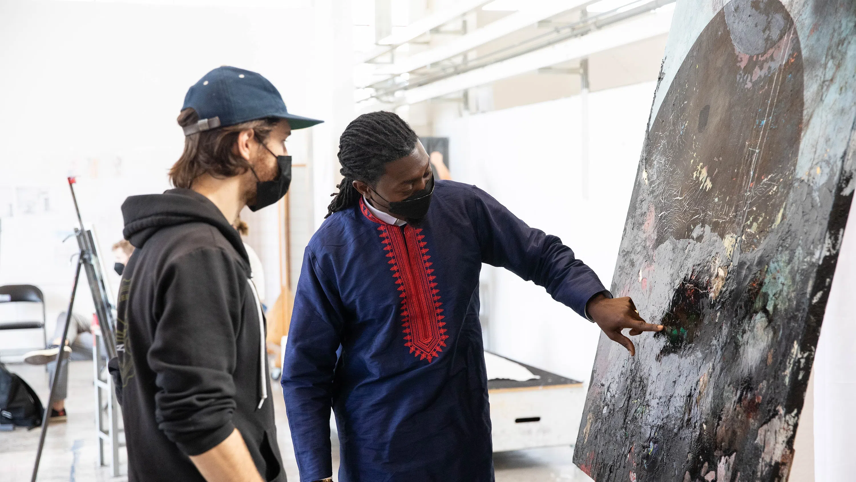 A faculty member points at a detail in a student’s painting.