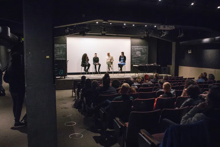 Four speakers sit on a stage in front of an audience. 