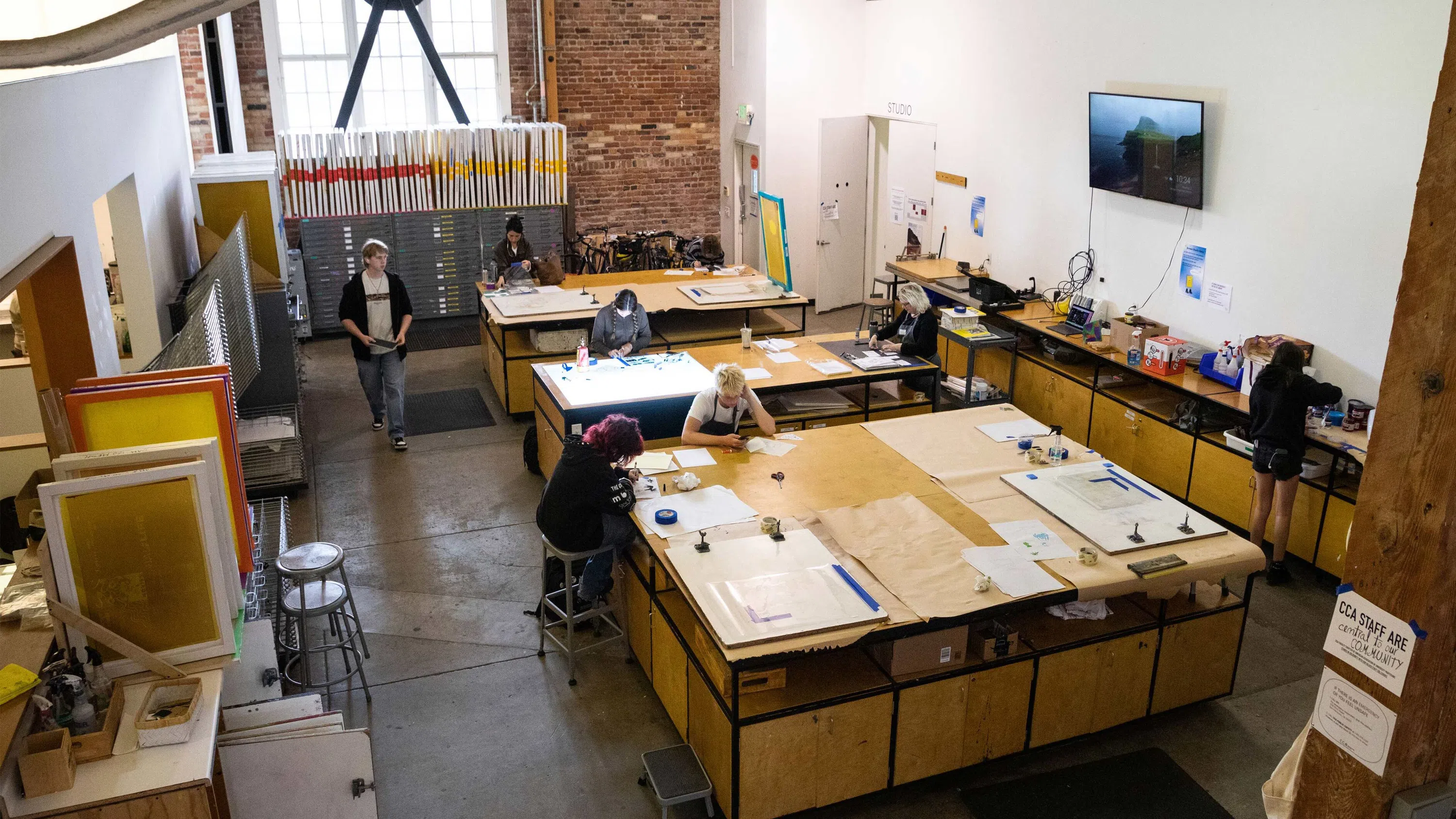 Overhead view of five students sitting at large tables working on photography and printmedia projects. 