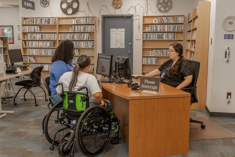 Two students being helped by a library staff member 