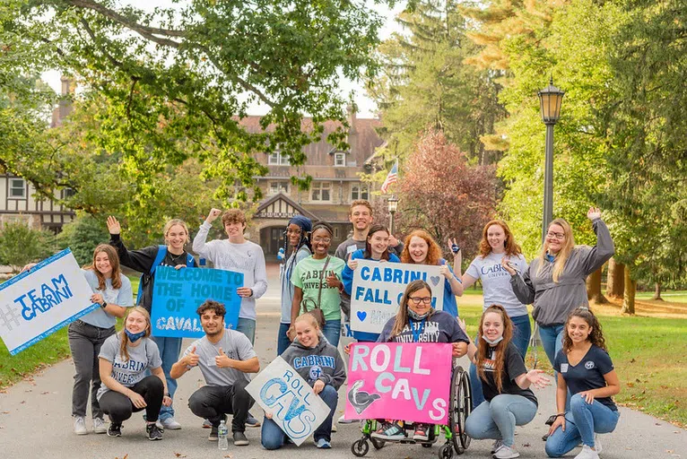 Group of students from all backgrounds hold signs outside to cheer on future cavaliers!