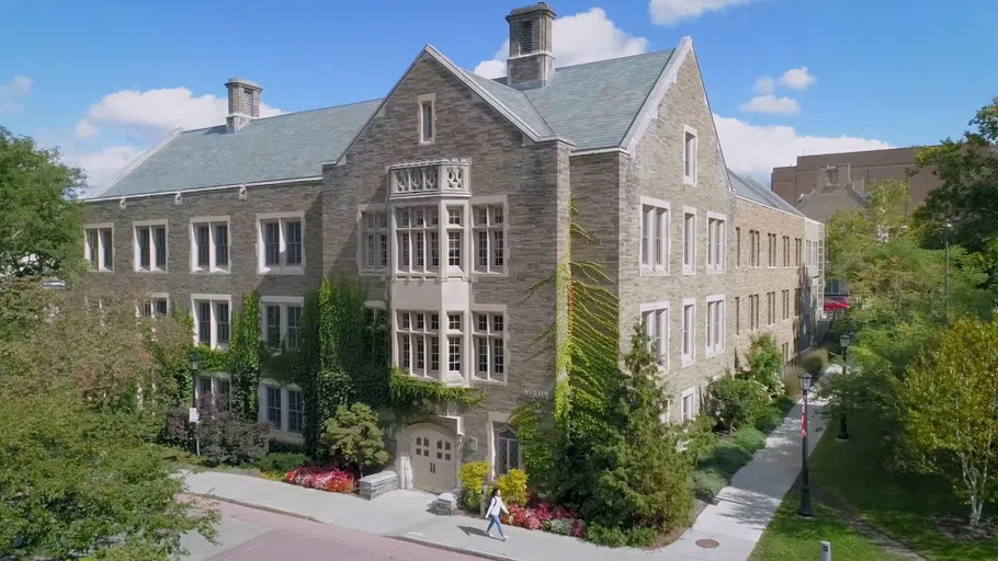 Ives Hall, a Collegiate Gothic-style building, as seen on a sunny day. Ivy grows on the building’s sides, with other lush vegetation surrounding it.