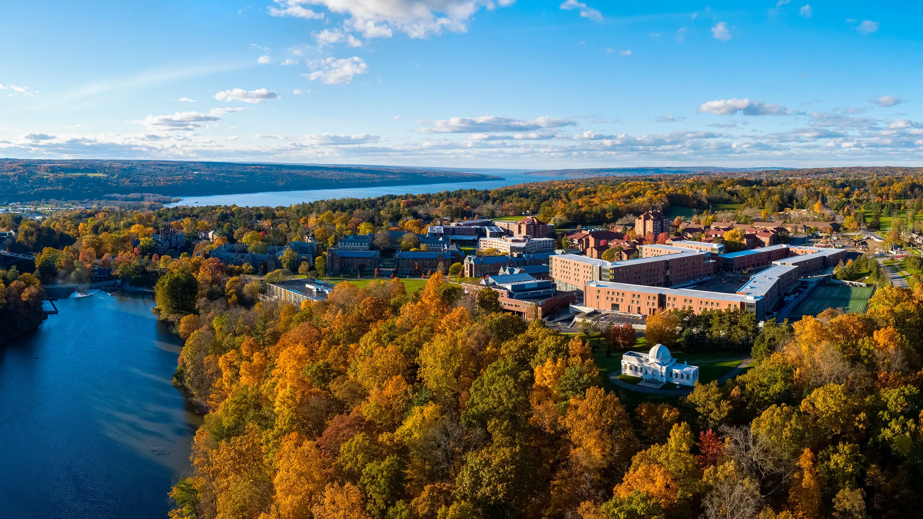 An aerial photo of the buildings of North Campus, with Beebe Lake at lower left and Cayuga Lake in the background.