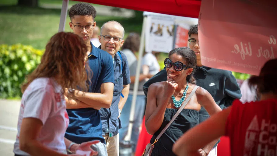 Five individuals are seen talking to each other, standing under a red 10x10-foot tent with a red top.