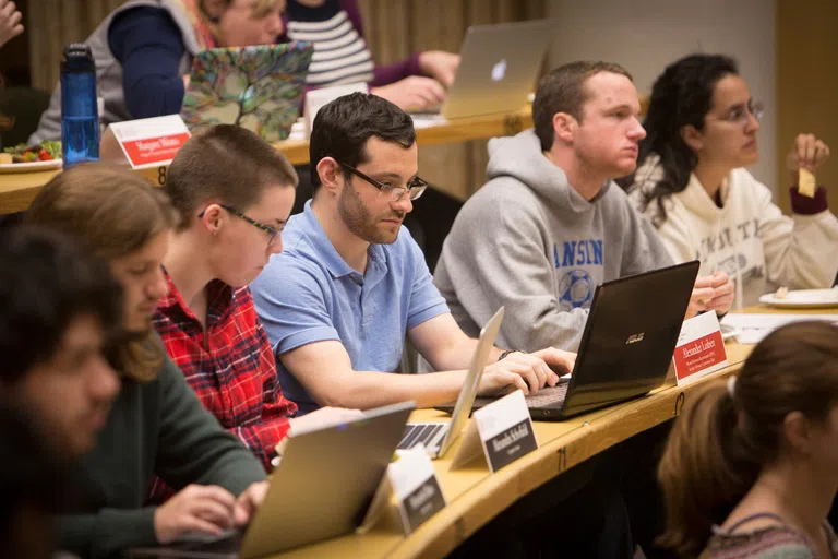 A row of students with laptops, in a classroom.