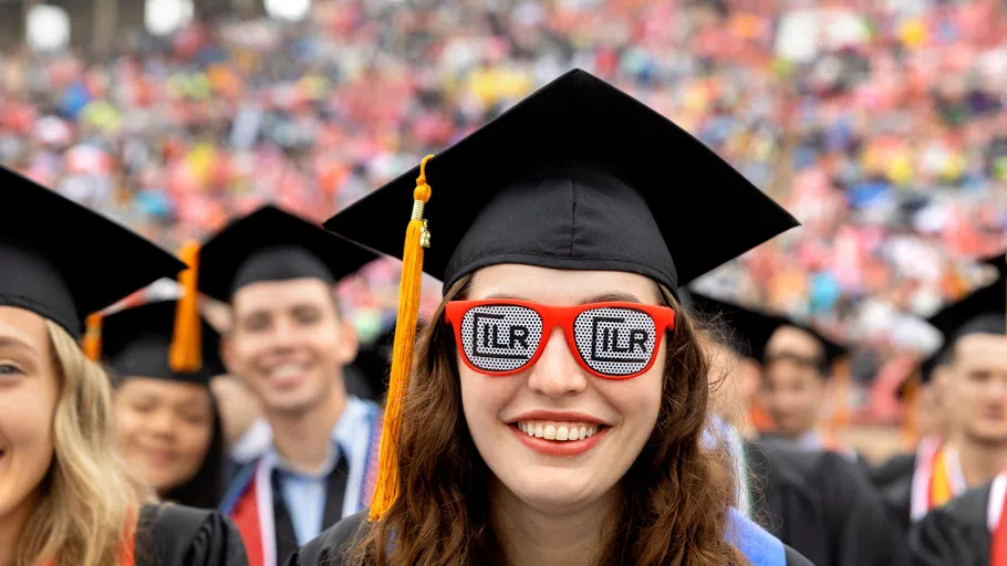 A student at Cornell’s Commencement ceremony wears sunglasses with red frames and the phrase “ILR” printed on each lens. 