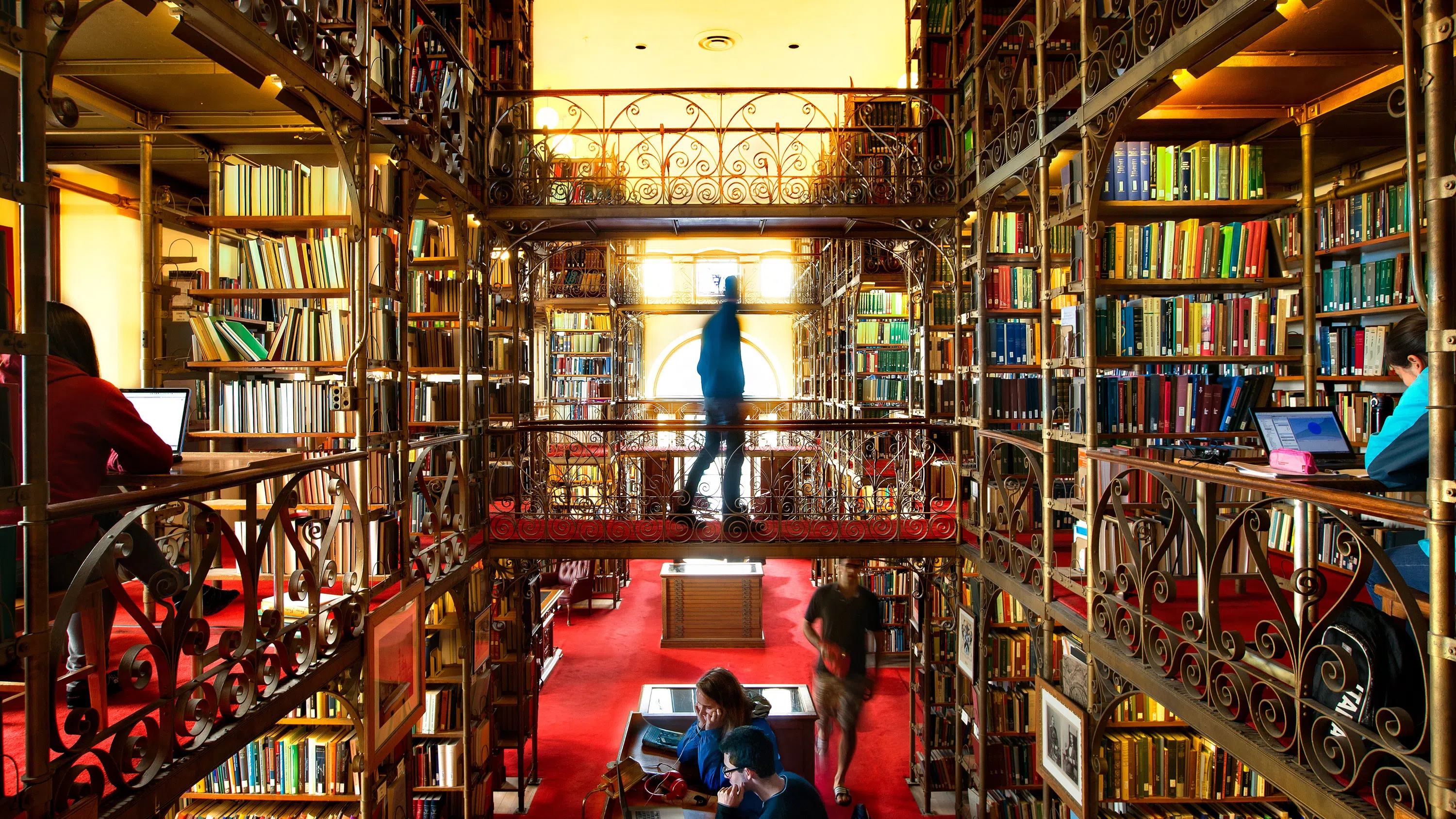 Wide shot of a person in silhouette walking between two multi-story library stacks.