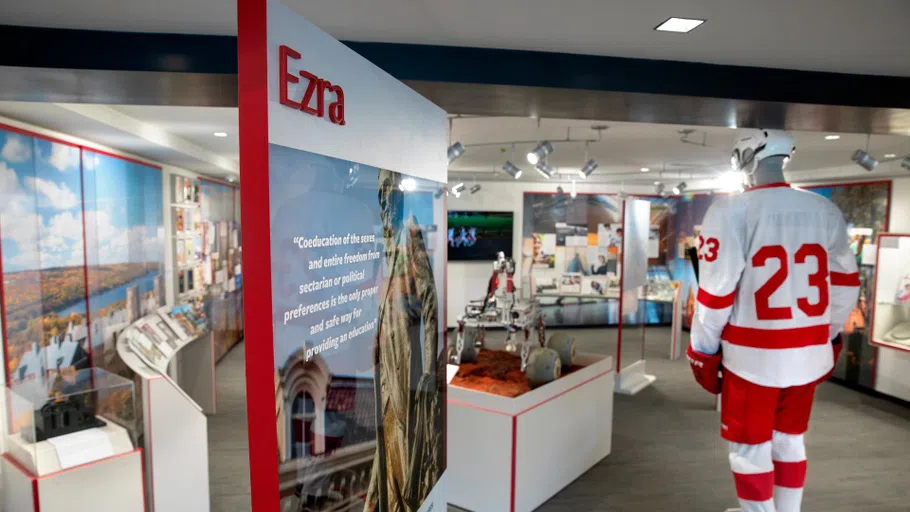 The Martin Y. Tang Welcome Center's history of Cornell artifacts. There is a vertical panel, about 6 feet tall, that says EZRA. Next to it is a mannequin wearing a Cornell hockey jersey.