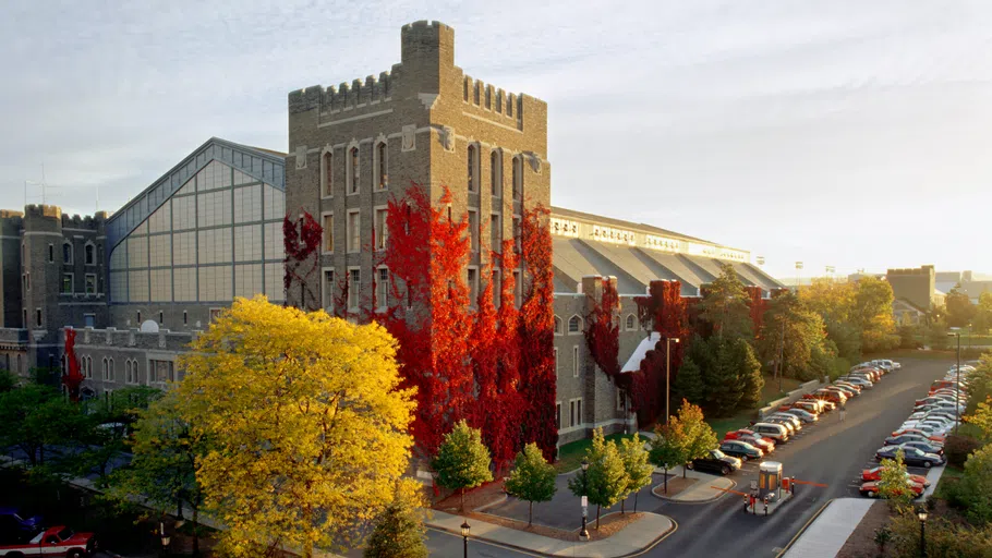 Exterior of Barton Hall, with autumn-colored red ivy climbing one side. A tree in the foreground is also bathed in yellow foliage.