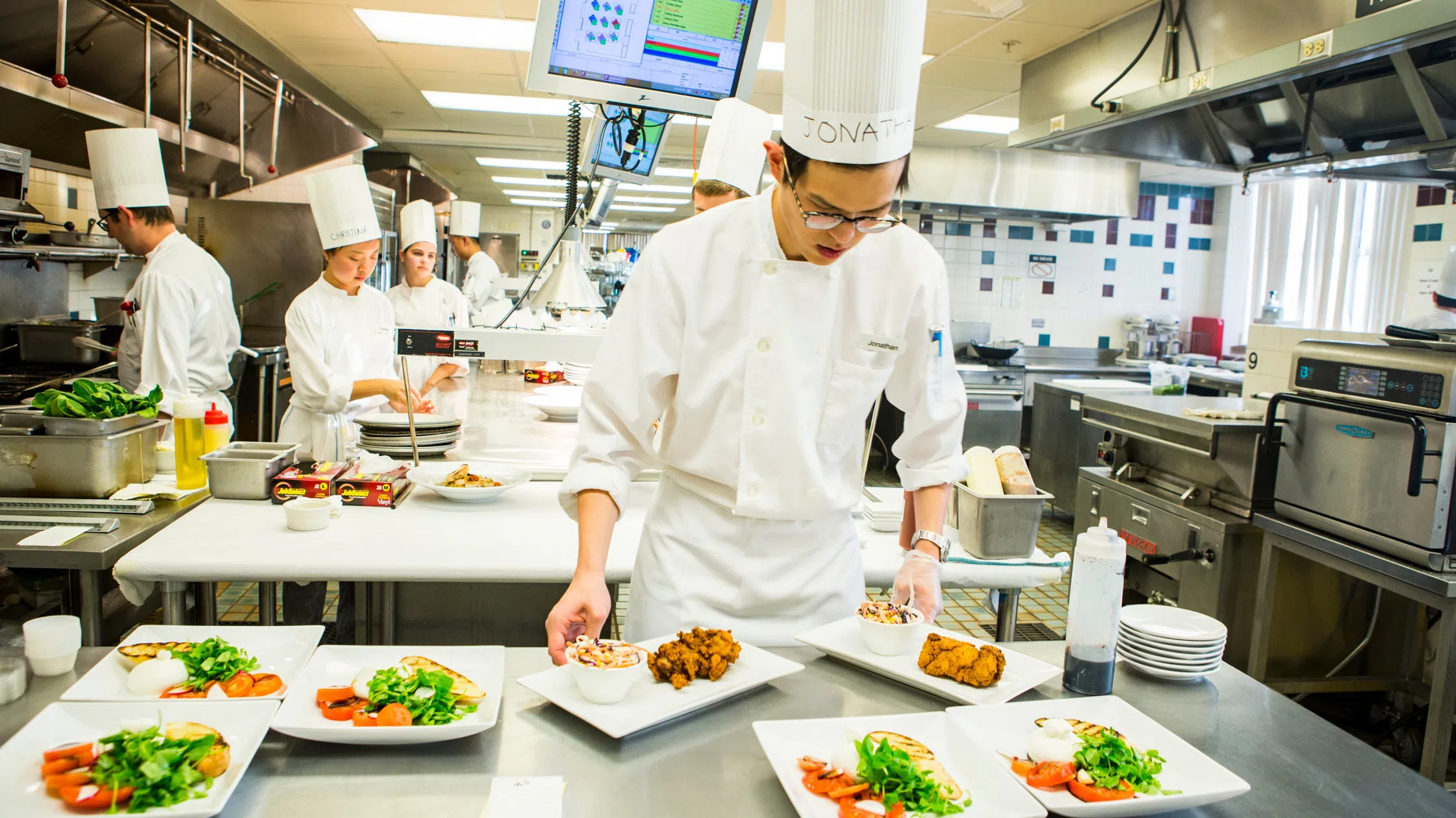 A student chef prepares several plates for a meal in Establishment at Statler, a hands-on learning environment. 