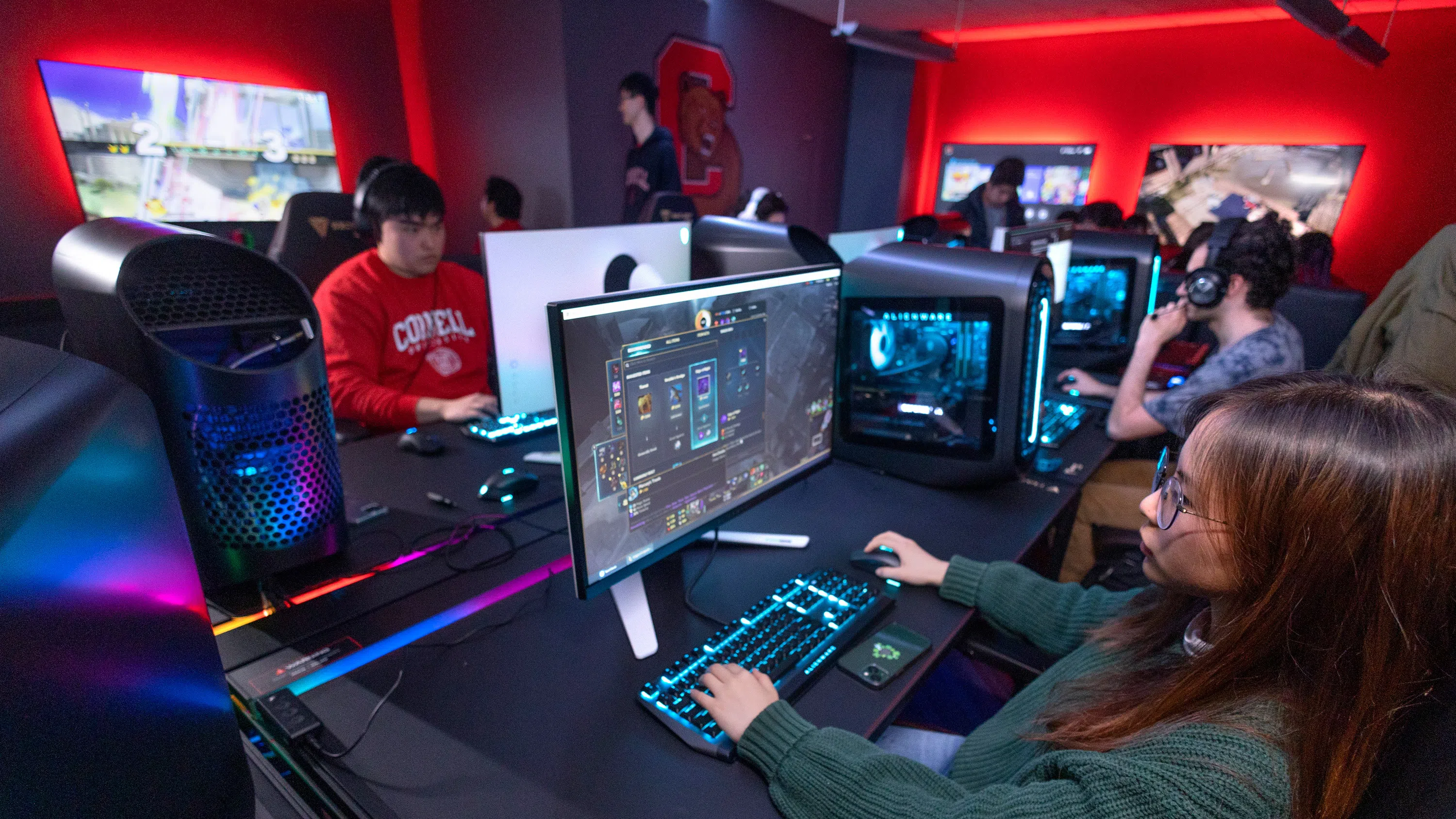 In the Esports Gaming Lounge, four students sit and stand near a console on the left, while a sole gamer uses a different console in the foreground, at right.