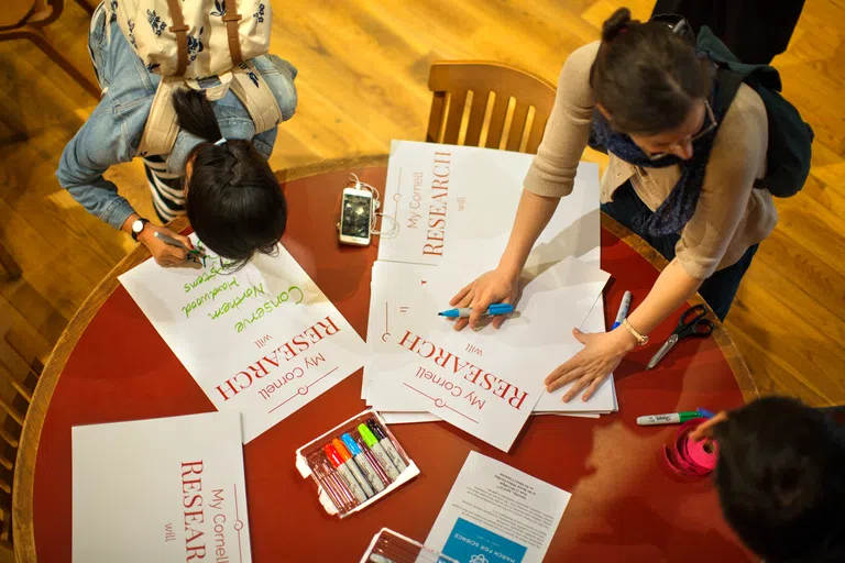 A closeup overhead shot of a table, with students’ hands seen holding assignment materials.