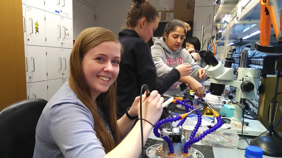 Several students work at a lab bench crowded with microscopes, helix models and other equipment.