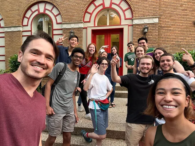 A large group of college students stands in front of a brown brick building in Washington, D.C.