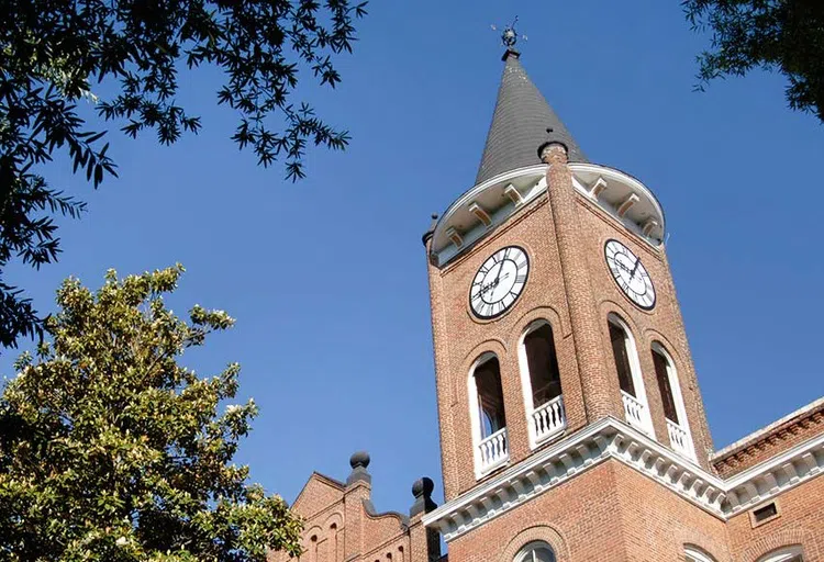 Spired top of a brick tower featuring a partial view of a clock.