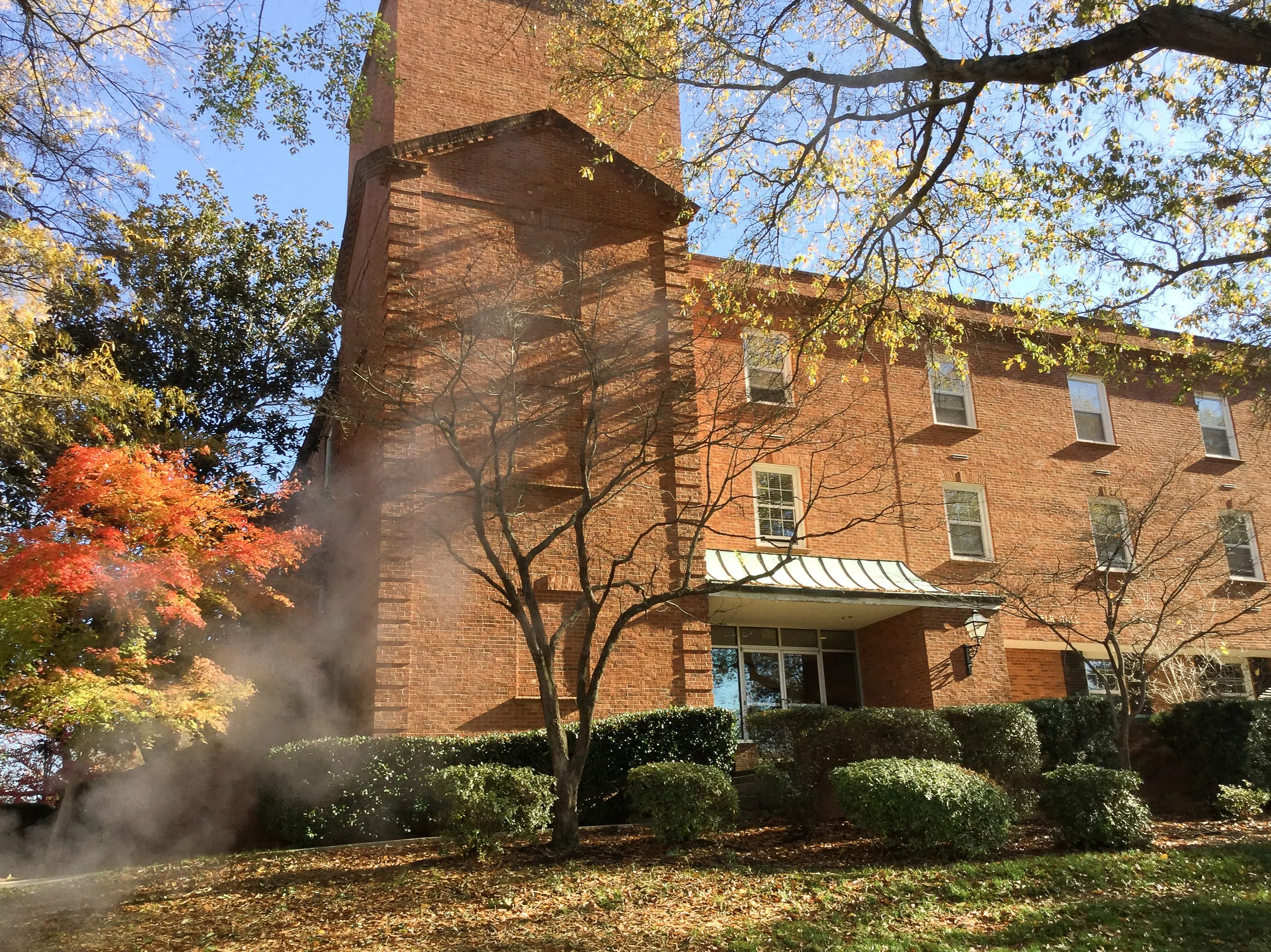 Three story brick building with grassy field in foreground.