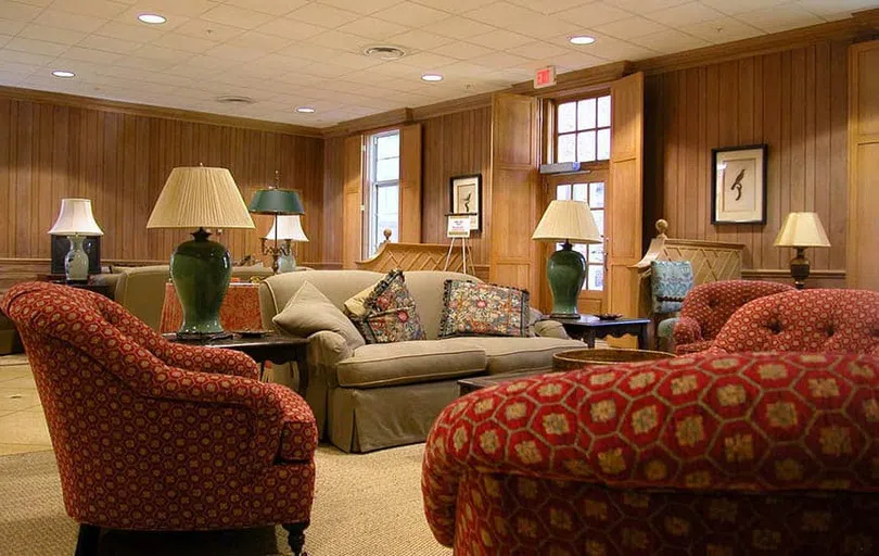 Two red chairs sit opposite a sofa between tables with lamps.