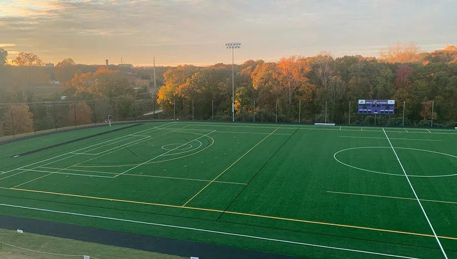 A green athletic field with white chalk lines is shown as the sunsets in the background to the leff.