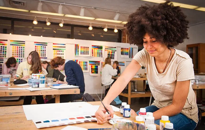 Adult students work at three at studio tables. Posters with bright colored squares hang on a wall in the background.