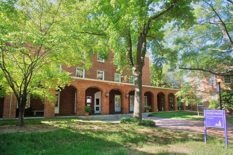 Three story brick building with eight brick arches leading to a covered porch. The words "Mickel Library" appear in gold letters above the center arches.