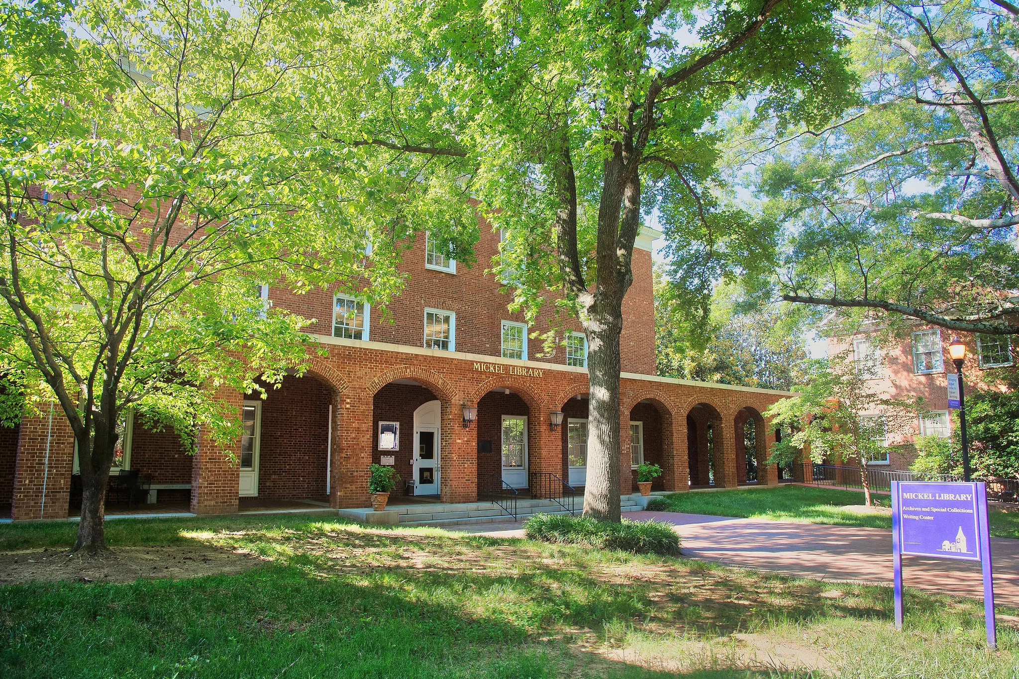Three story brick building with eight brick arches leading to a covered porch. The words "Mickel Library" appear in gold letters above the center arches.