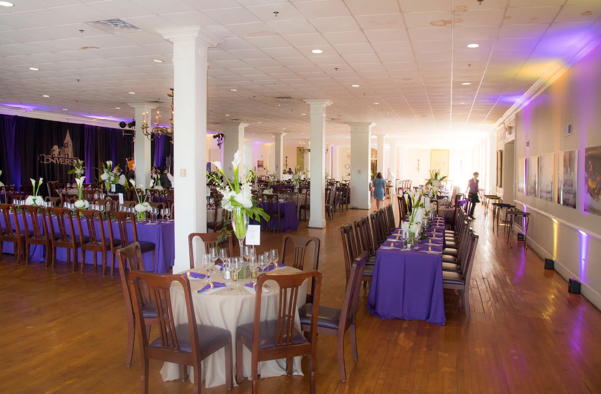 Purple and white draped tables with wooden chairs line a large dining room with white columns. The Converse logo can be seen on drapery in the background.