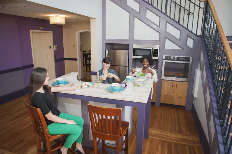 Three students prepare food in a kitchen.