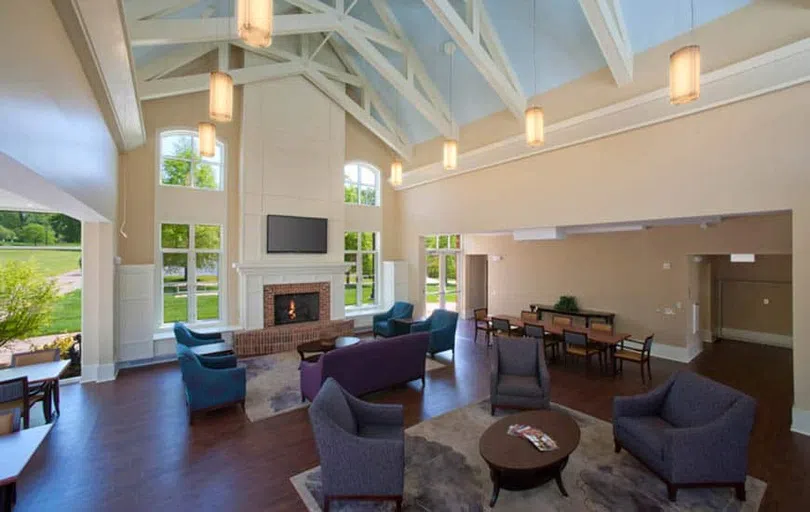 A vaulted room full of couches and chairs focuses on a brick fireplace flanked by tall windows on each side.