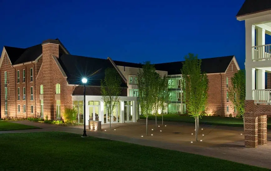 Front entrance to a two story building at night with light shining from the windows and a streetlight in the foreground.