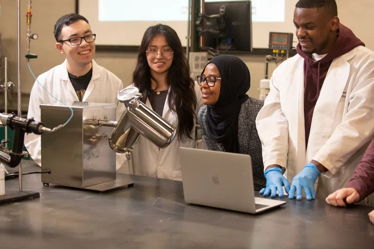 Students and a professor observe machinery in a lab