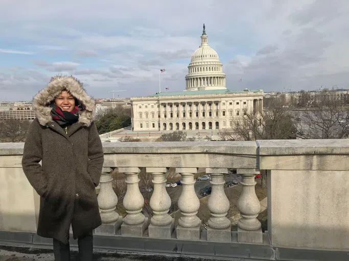 a woman in a jacket stands on a bridge overlooking the Capitol Building