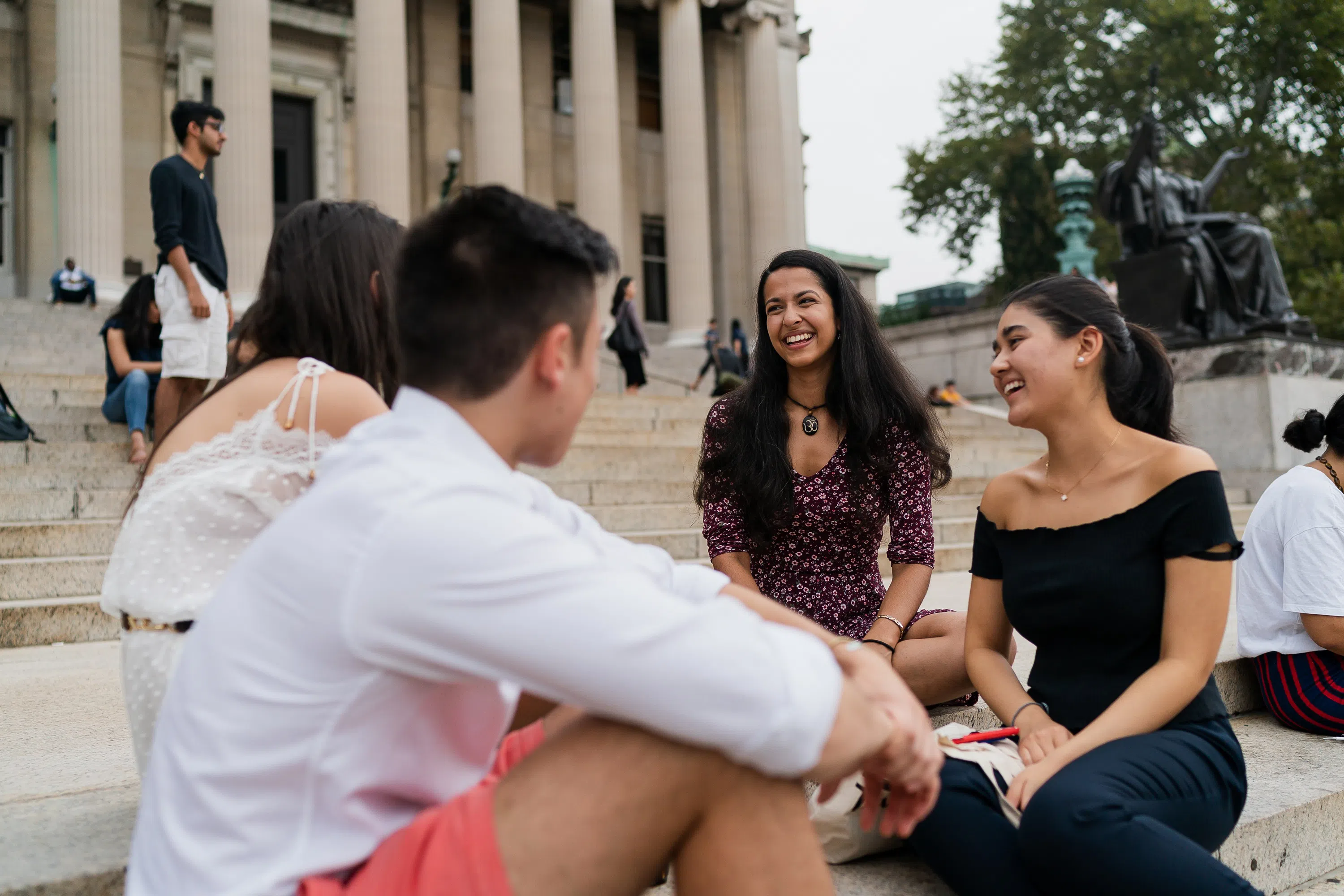 Four students sitting on stone steps talking and laughing in a circle.