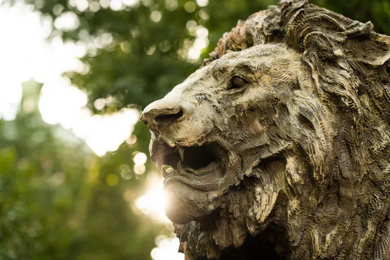 Close up of a bronze statue of a lion's head with trees in the background