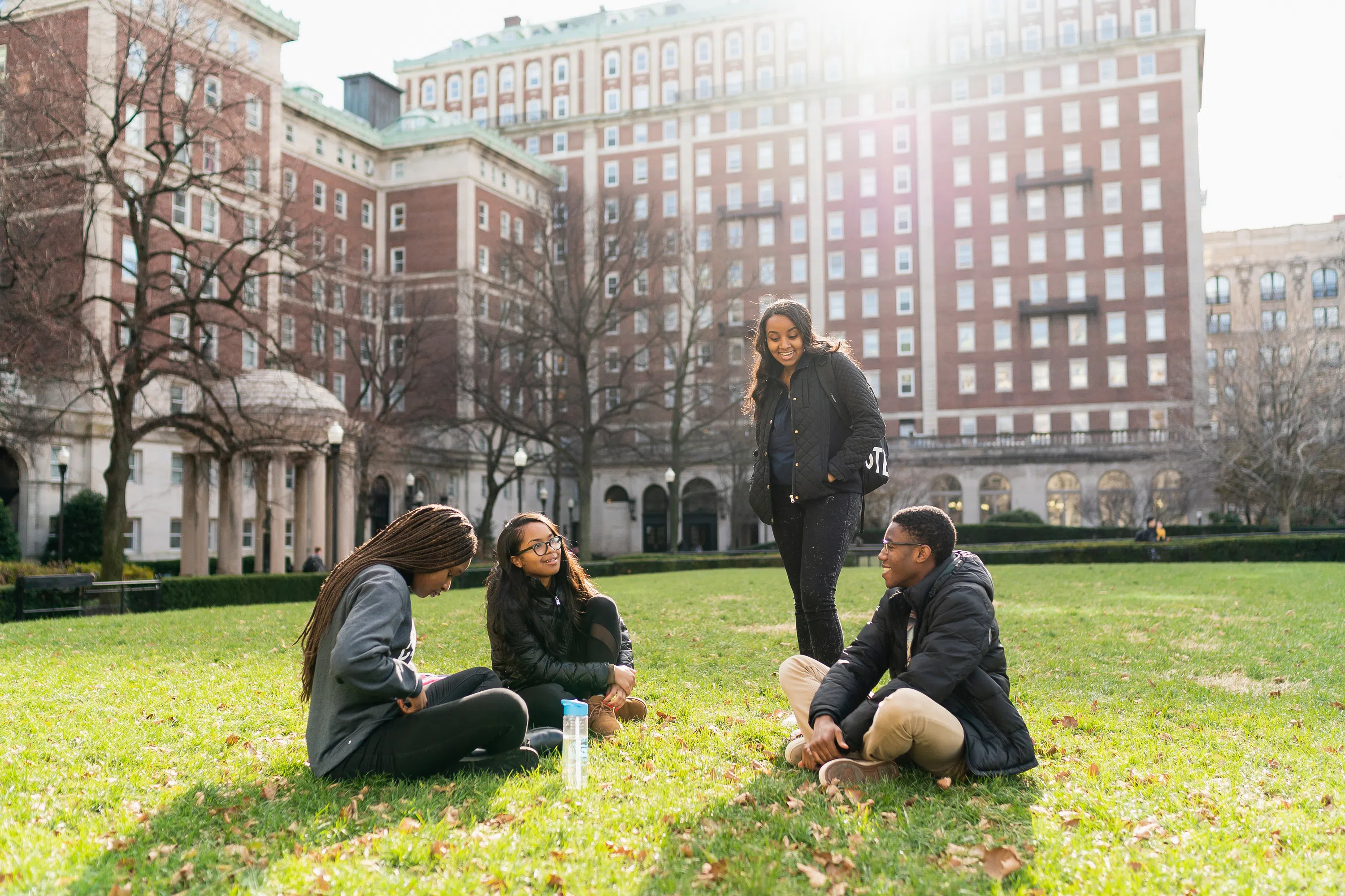 4 students gather on the green lawn with the residence halls in the background.