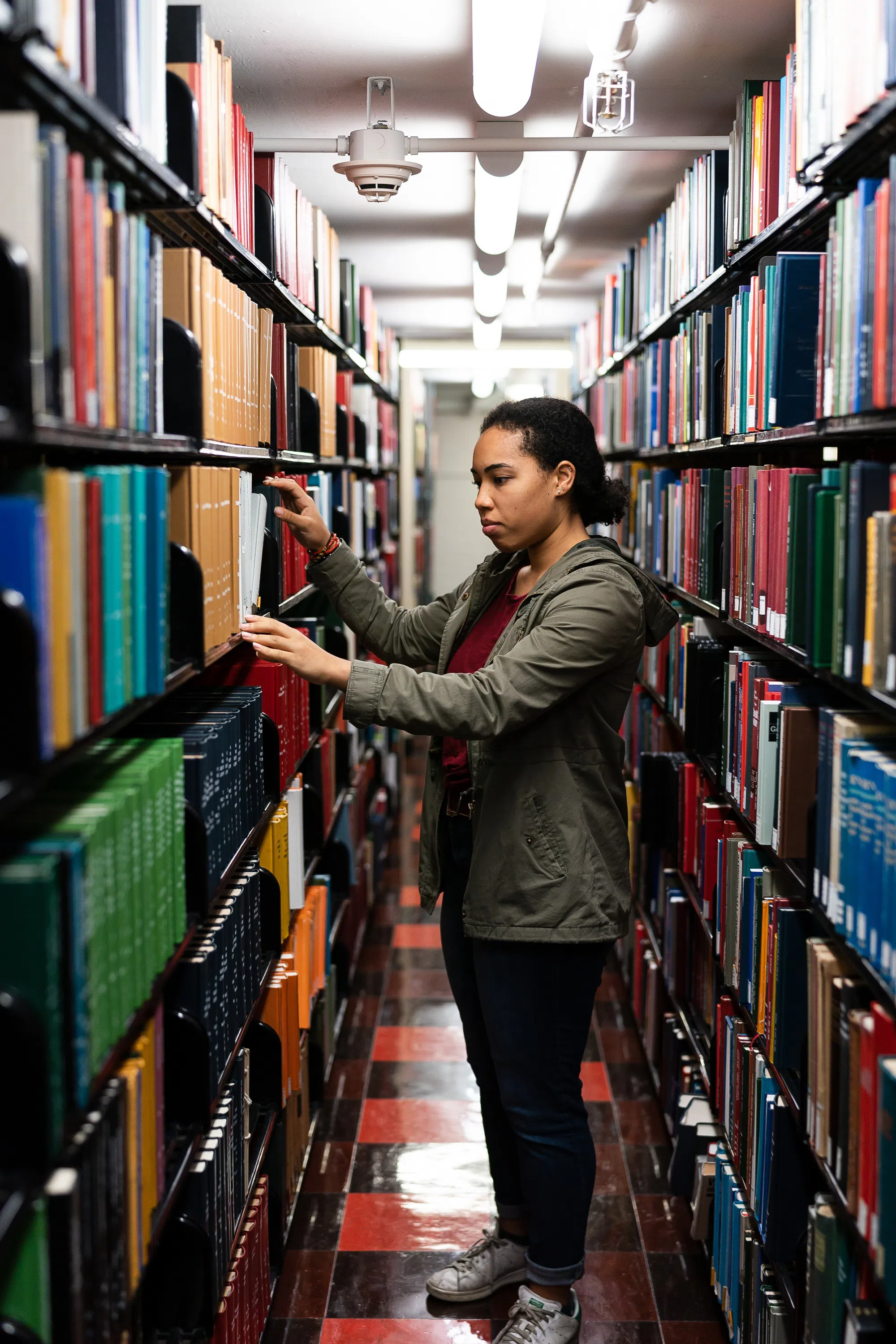 A young female students stands in the library looking at books.