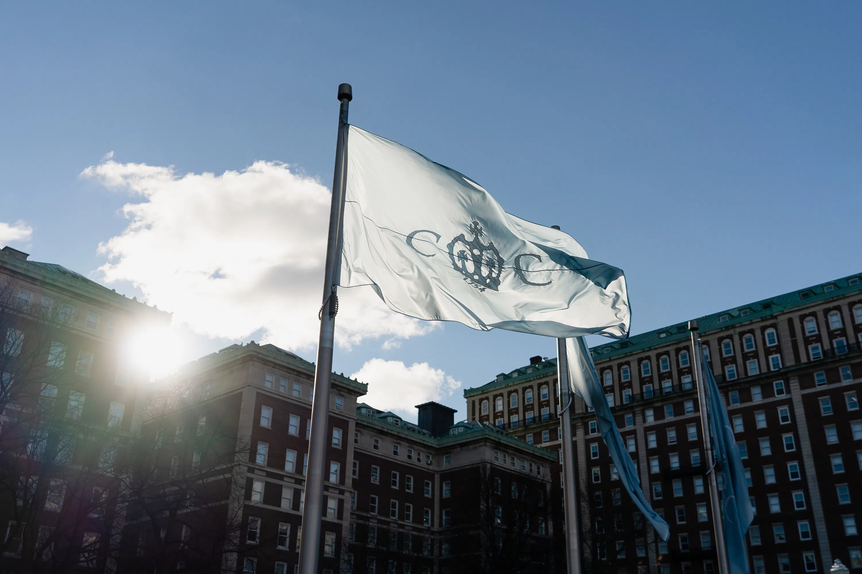 A light blue Columbia College flag flies in the wind with residence halls in the background.