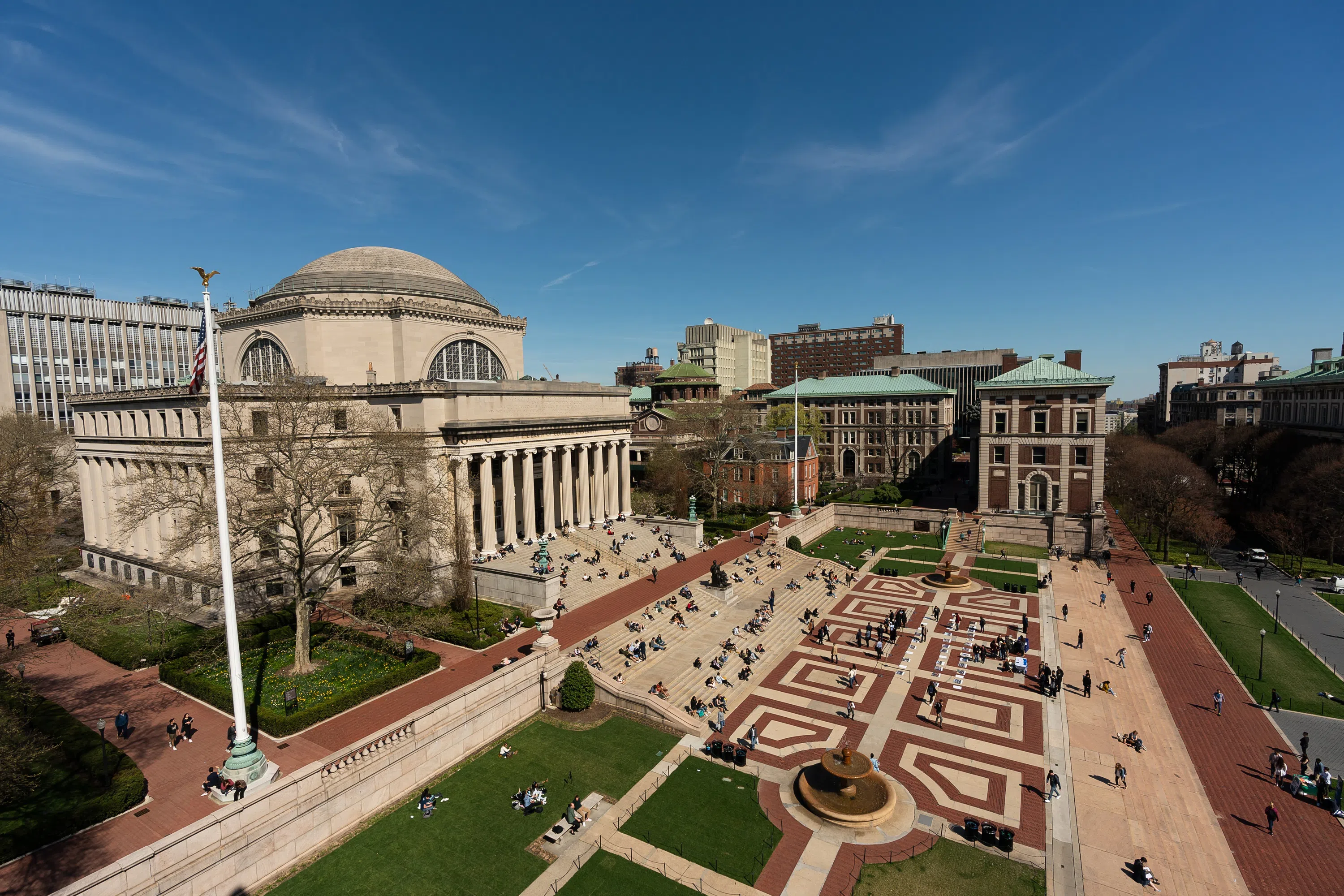 An aerial view of Low Library, a large dome shaped building with a set of stairs in front. Students are scattered across the quad.