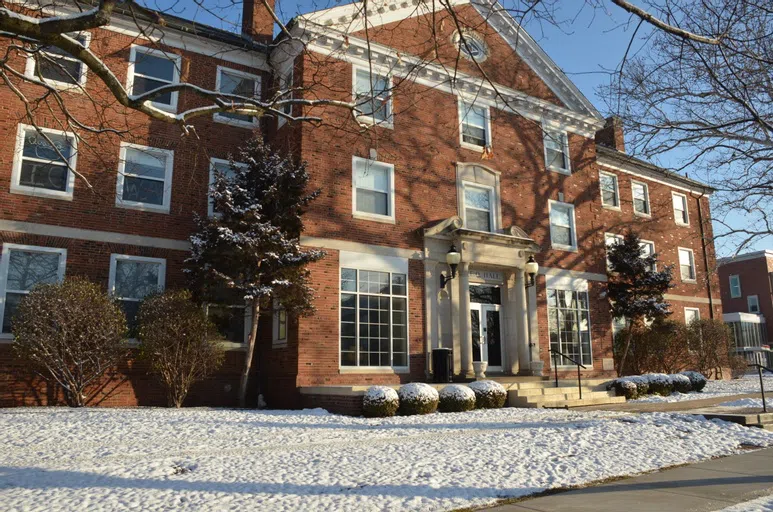 Snow on the ground, bushes, and tree branches makes the front of this residence hall look like a winter wonderland