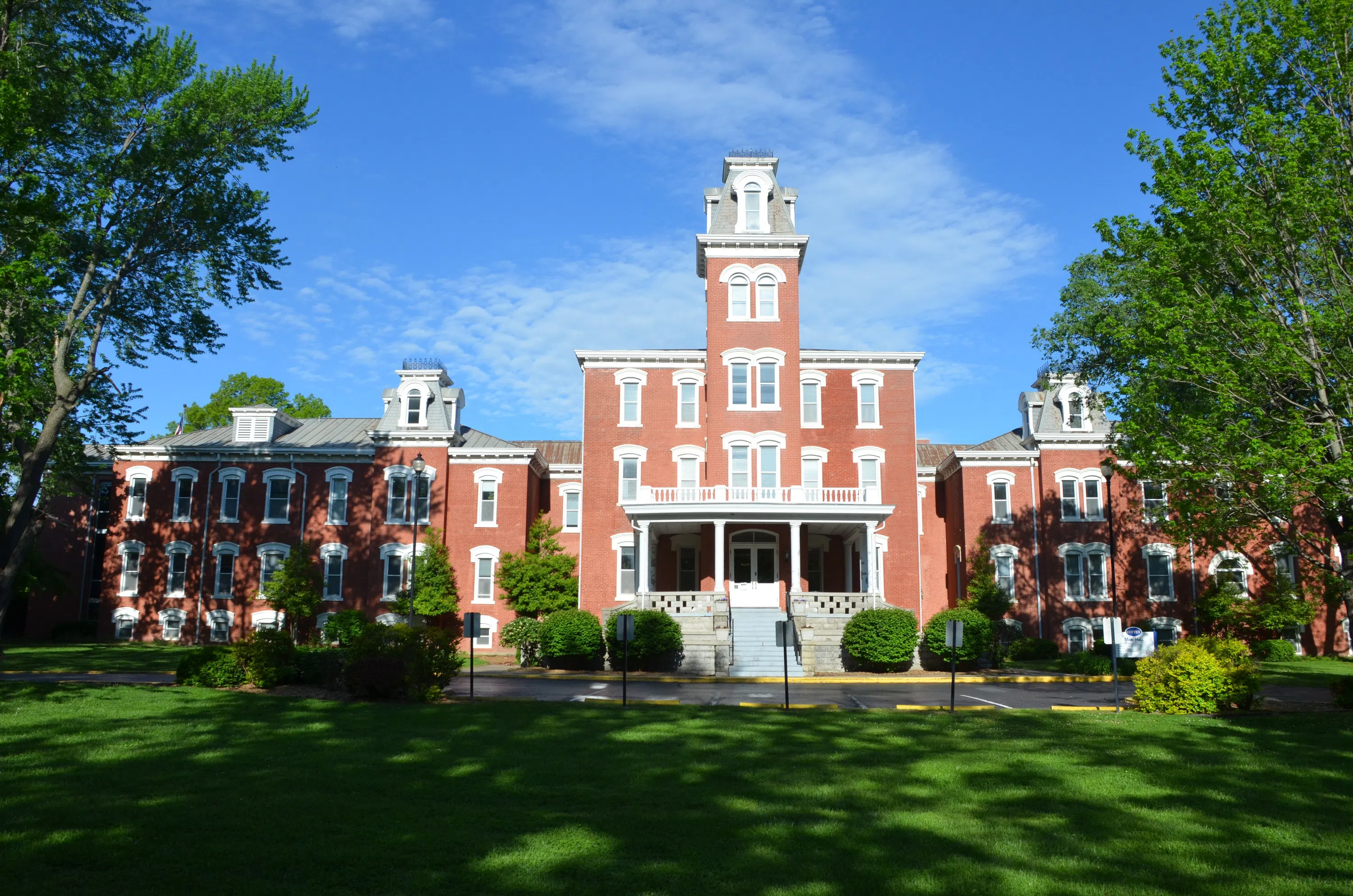 An enormous brick building with a two wings on either side. The lawn in front is vibrant and manicured, while the sky behind is deep blue with some delicate clouds