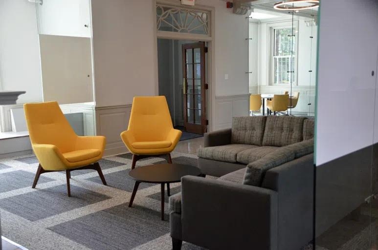 Chairs in Cottey yellow, couches, and glass panels separating the spaces make this residence hall lobby modern and chic