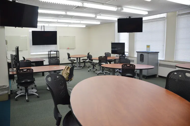 Round tables, monitors, and a large cart with MacBooks locked inside