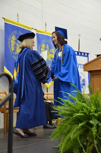 The president of the college, in full regalia, congratulates a new graduate with a smile and handshake