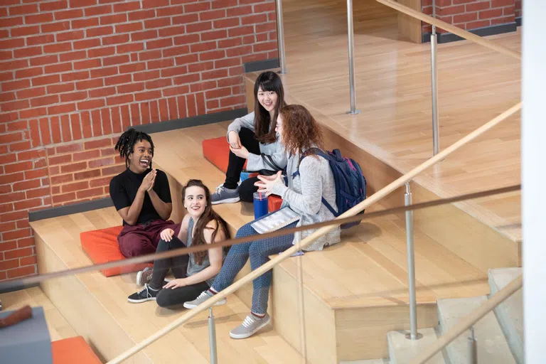 Students hanging out on the large wooden stairs of the lobby. They are laughing and enjoying the atmoshpere