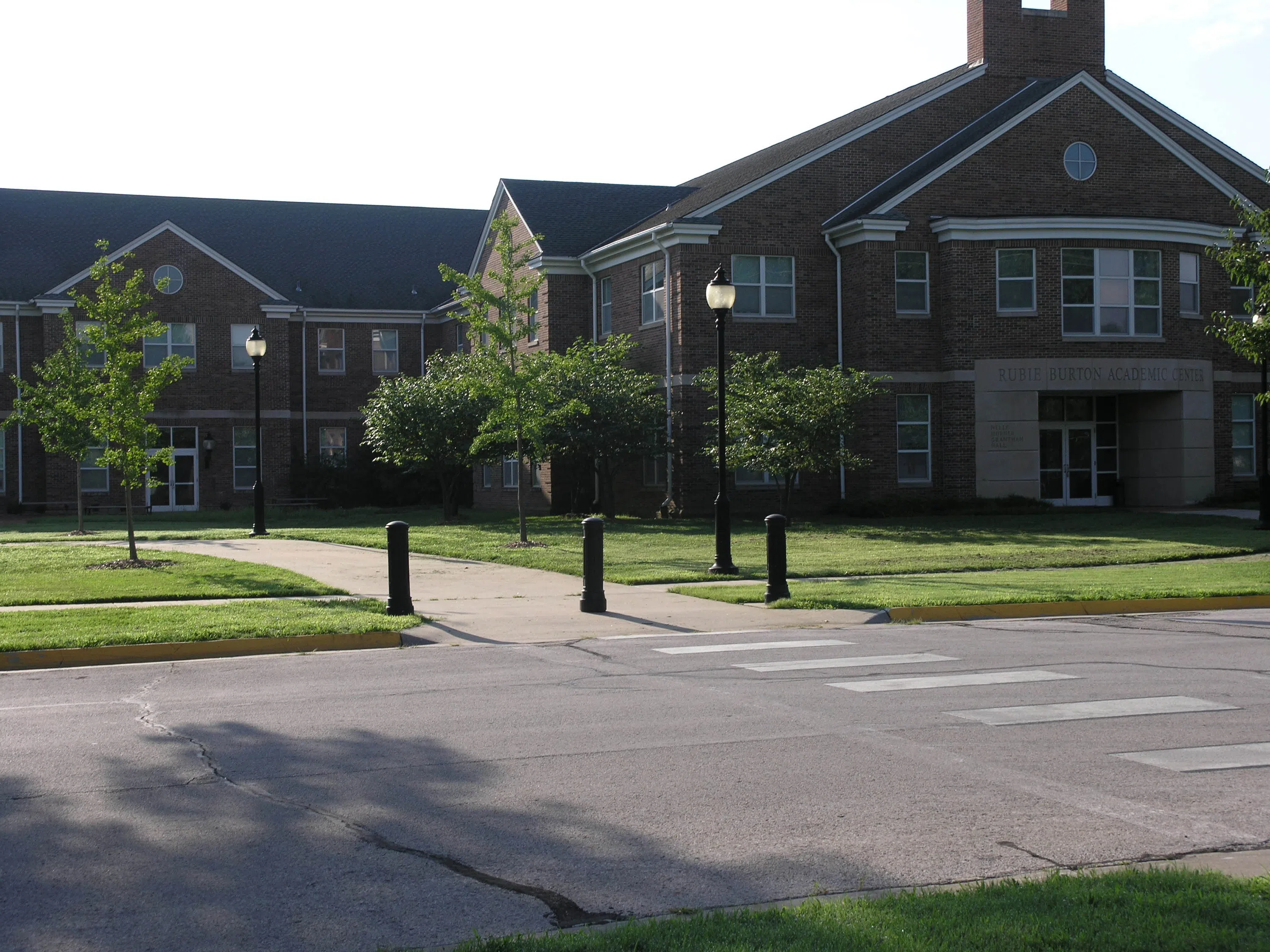 A large brick building shaped like an 'L,' lined with trees, sidewalks, and vibrant grass