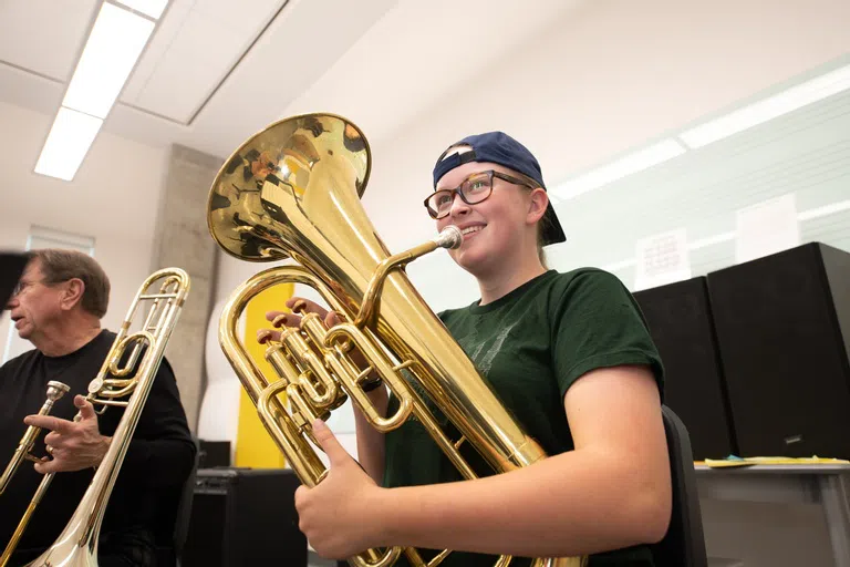 A student smiles as she takes a break from playing the tuba beside a professor