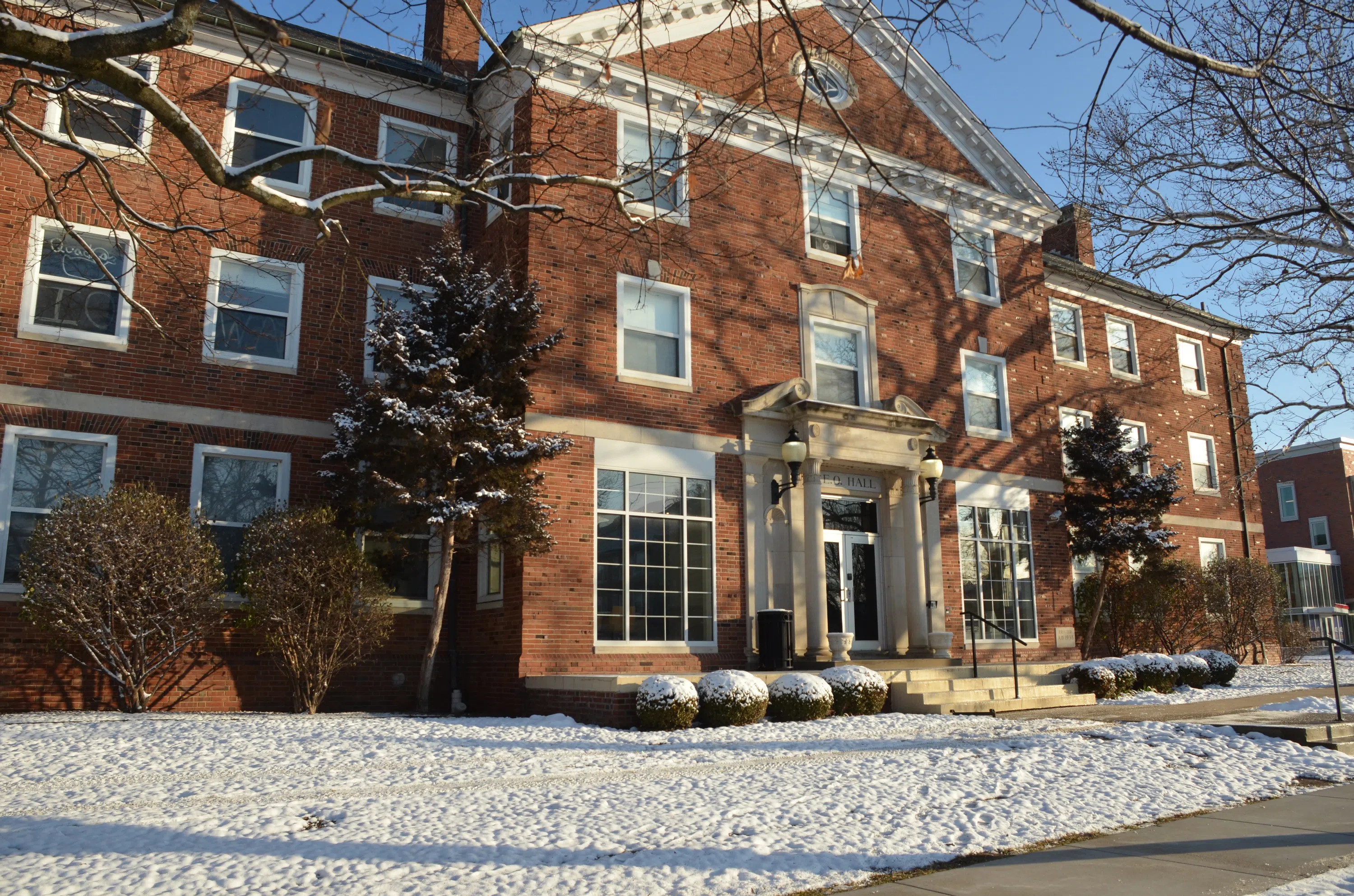 Snow on the ground, bushes, and tree branches makes the front of this residence hall look like a winter wonderland