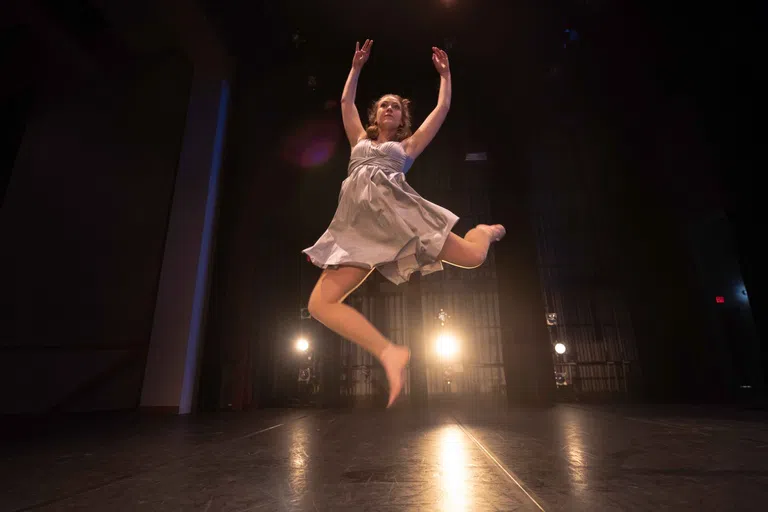 A dance student gracefully flying through the air, with etherical backlighting on a dark stage