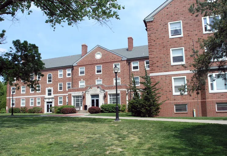 A variety of tree types, differently-colored bushes, and tall light posts set this dorm's front facade apart